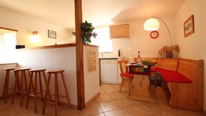 Een keuken met houten krukken, een eettafel met rode kussens en een houten bank.