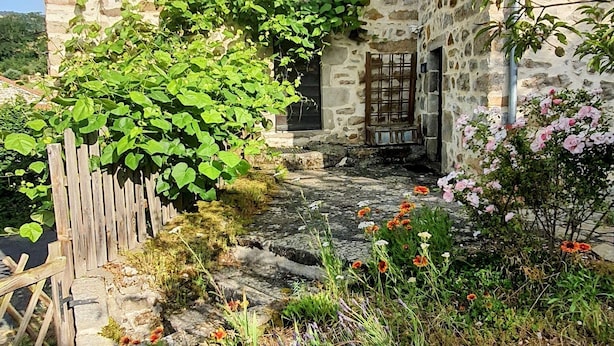 Een stenen gebouw met een houten deur, een raam en een kleine tuin met bloemen en planten.