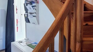 Een houten trap die naar een verdieping leidt, een wit bureau met papieren en een deur met een rode hendel.