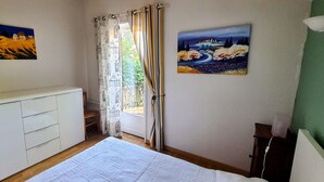 Een slaapkamer met een bed, een kledingkast, een schilderij aan de muur en een raam met gordijnen.
