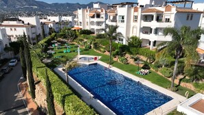 A residential area with a swimming pool surrounded by greenery and white buildings with balconies.