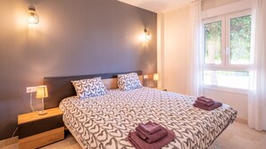 A bedroom with a large bed, two bedside lamps, a nightstand, and a window with curtains.
