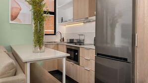 A modern kitchen with wooden cabinets, a stainless steel refrigerator, a dishwasher, and a small dining table with a plant. - Central Sea Point Studio | Rooftop Pool (Cape Town)