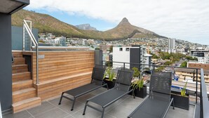 A rooftop terrace with a view of a mountain, wooden steps, and modern outdoor seating. - Central Sea Point Studio | Rooftop Pool (Cape Town)