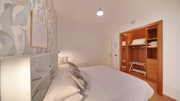 A bedroom with a bed, a wardrobe, a radiator, and a light fixture.