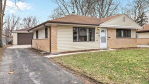 Une maison de plain-pied avec un garage, une porte d’entrée et un petit jardin devant.