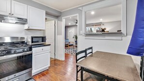 Une cuisine compacte avec des meubles blancs, une cuisinière et un four à micro-ondes. On y trouve une table à manger avec des chaises.