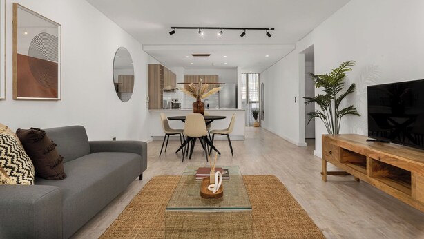 Ein modernes Wohnzimmer mit einem grauen Sofa, einem Glastisch und einer Holz-TV-Konsole.
