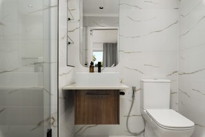 A modern bathroom with a marble backsplash, a wooden cabinet, a white sink, and a toilet.