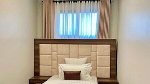 A modern bedroom with a large bed, a headboard, bedside tables, and a window with curtains. - Penthouse, (Kampala)