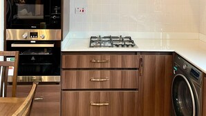 A modern kitchen with wooden cabinets, a built-in microwave, an oven, a gas stove, and a washing machine. - Penthouse, (Kampala)