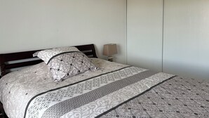 A neatly made bed with patterned bedding, a bedside lamp, and a closed wardrobe. - 20 mns from beaches and center of St Raphaël.2 50m2 type with nice terrace. (Saint-Raphaël)