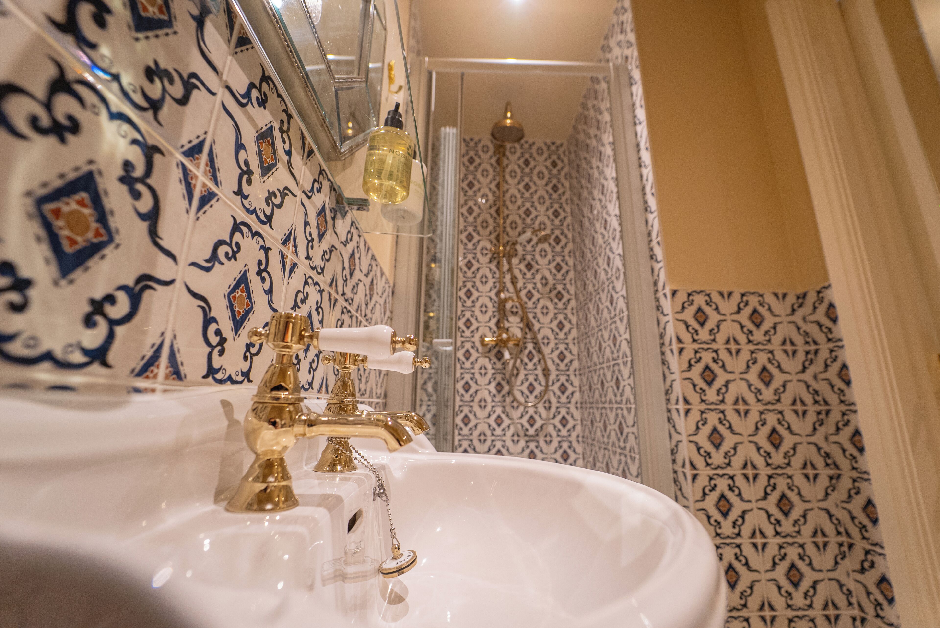 A bathroom with a white sink, gold faucets, and patterned tiles.