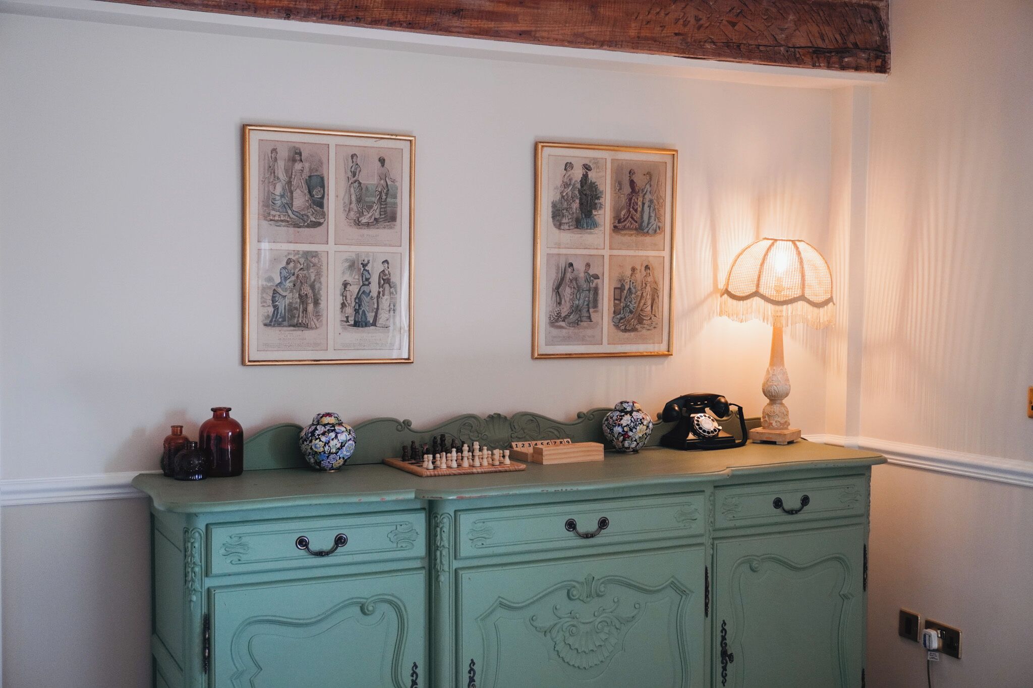 A room with a green dresser, a lamp, and two framed pictures on the wall.