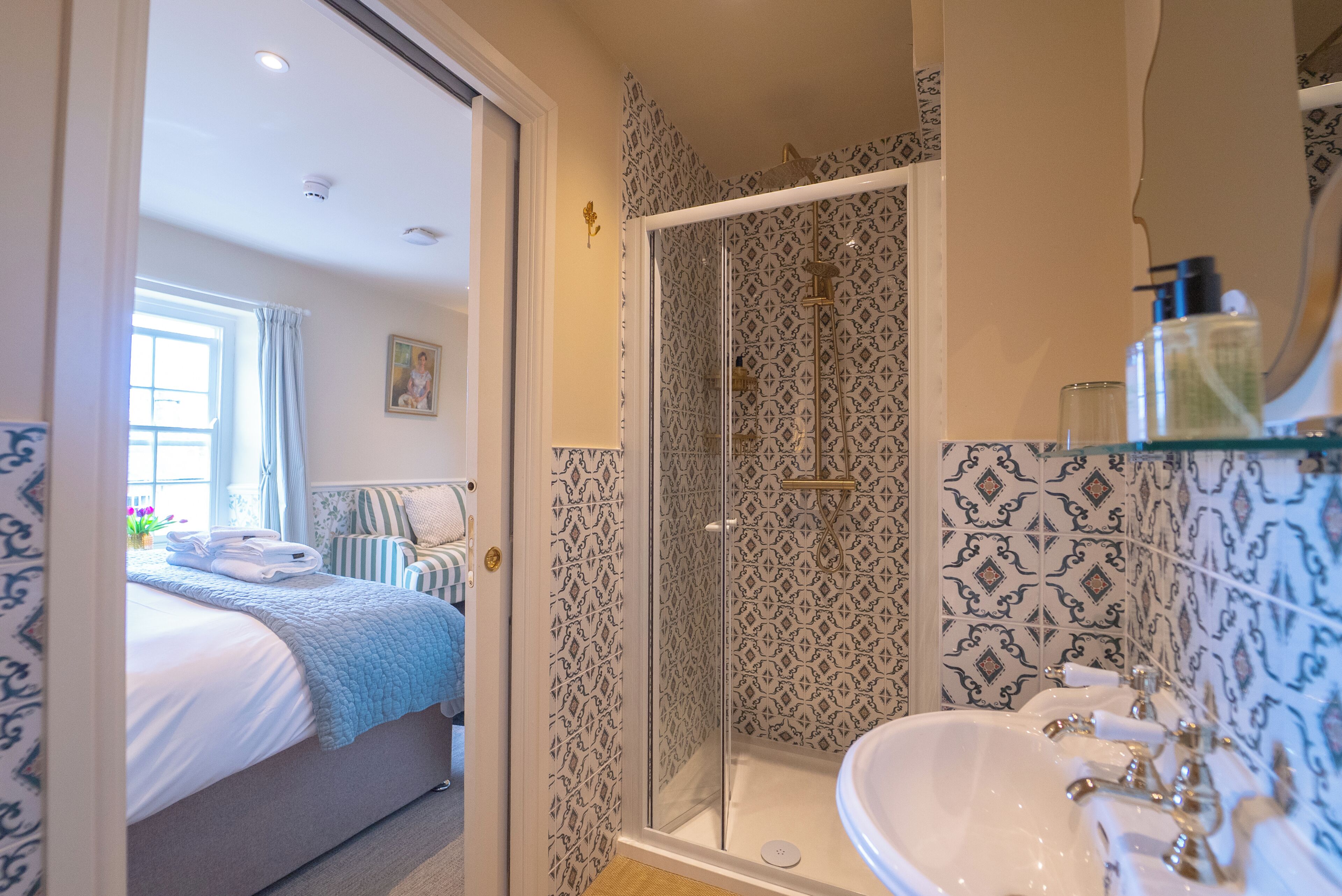 A hotel room with a bed, a shower with a glass door, and a bathroom with a sink and mirror.