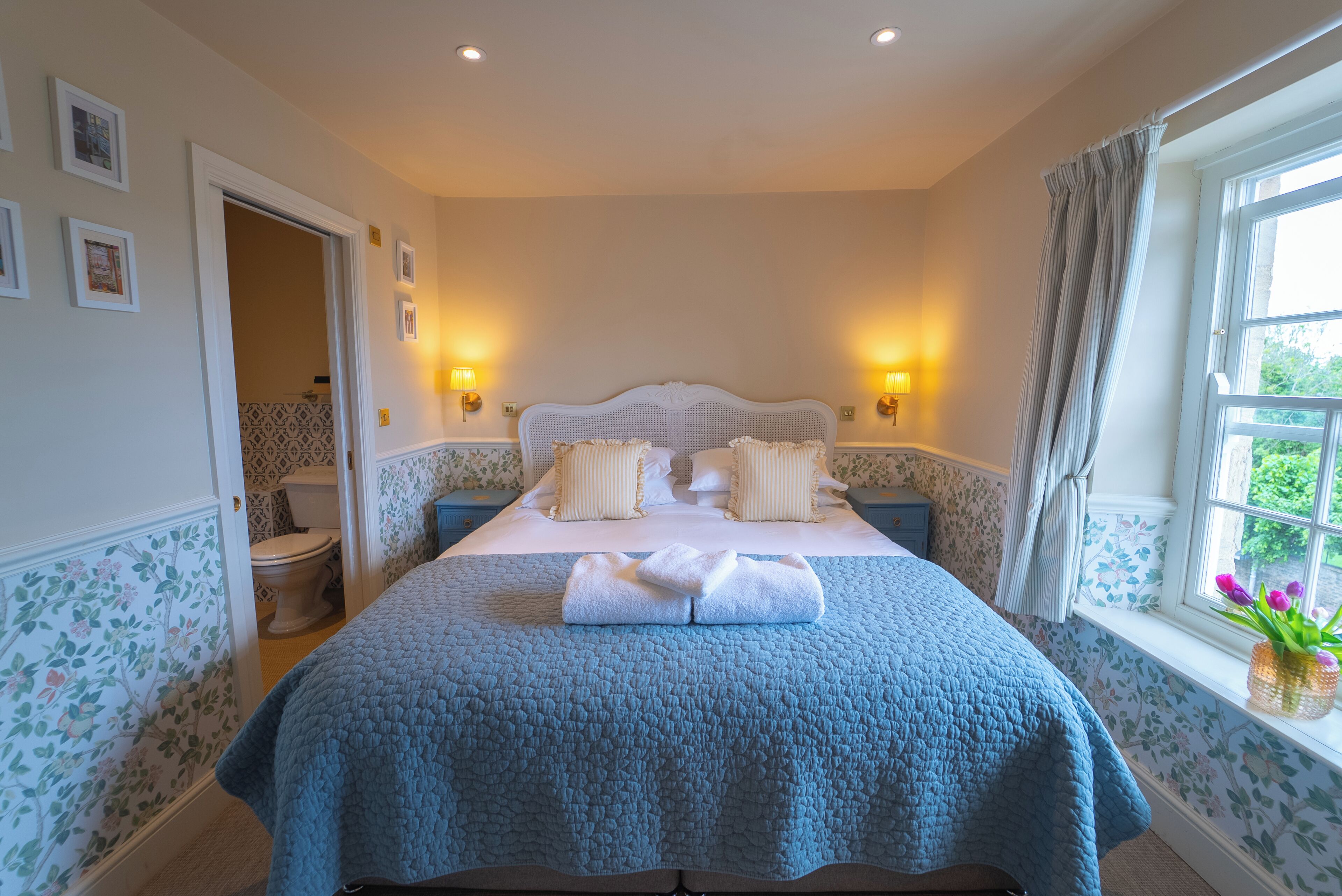 Un dormitorio con cama, lámparas de noche, una ventana con cortinas y vistas al exterior.