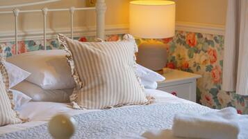 A neatly made bed with pillows and a blanket, a bedside lamp, and a floral wallpaper.