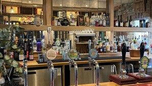 A bar area with multiple beer taps, a variety of bottles, and hanging wine glasses. - The Market Tavern (Bampton)