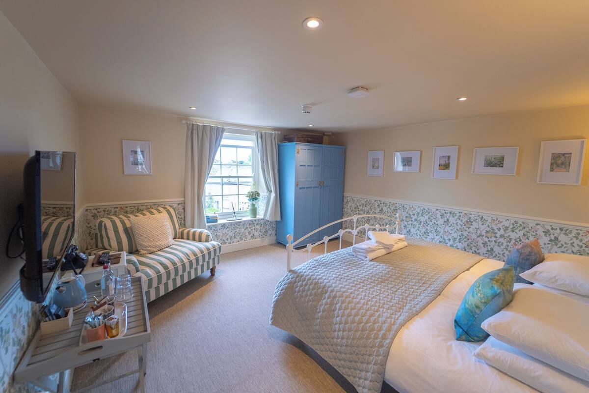 Un dormitorio con cama, sofá, una mesita, armario y ventana con cortinas.