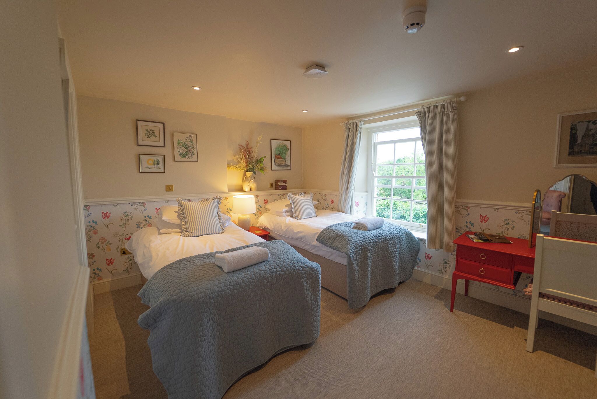 A bedroom with two beds, a desk, and a window.