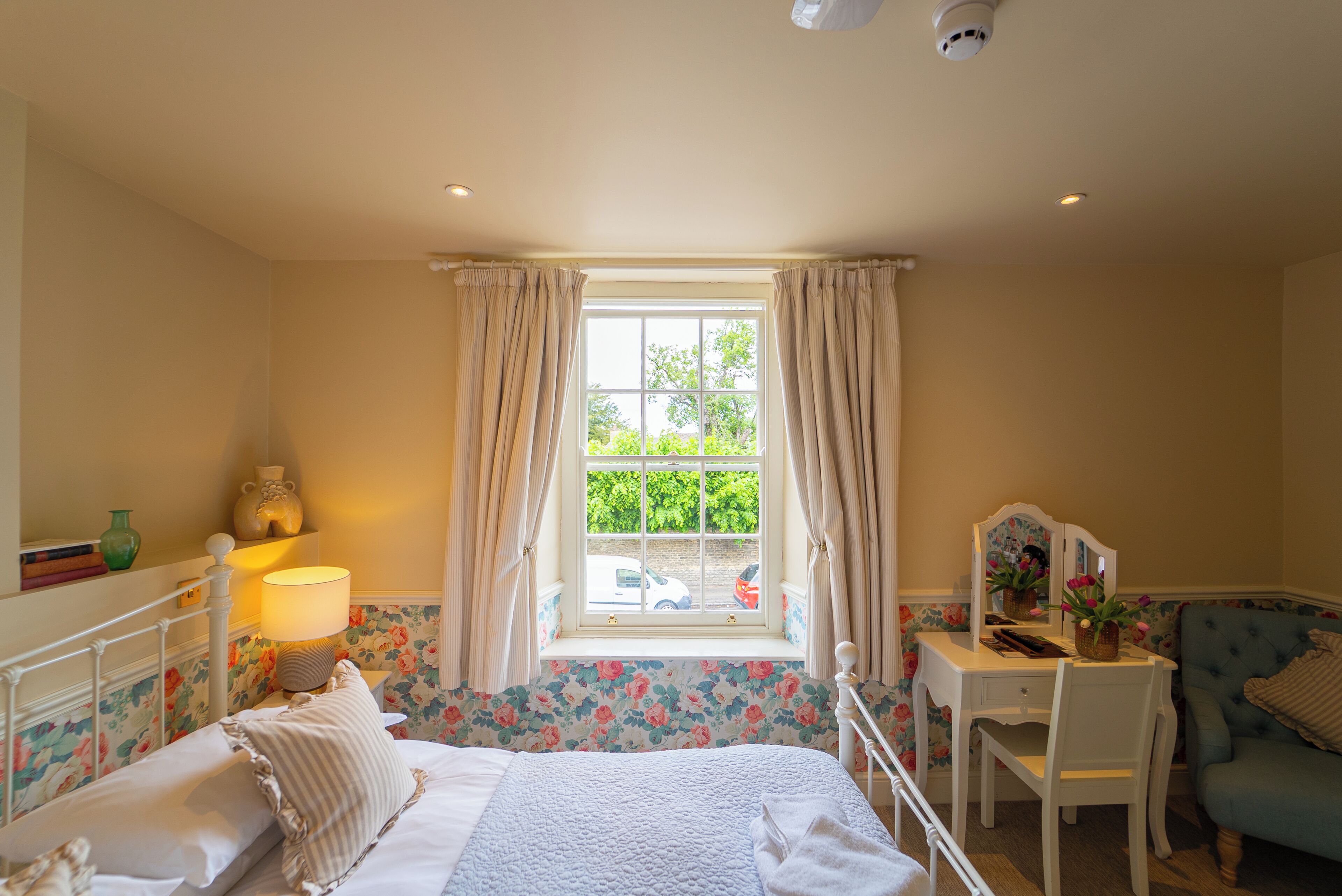 A bedroom with a bed, a desk, a chair, a window with curtains, and a lamp.