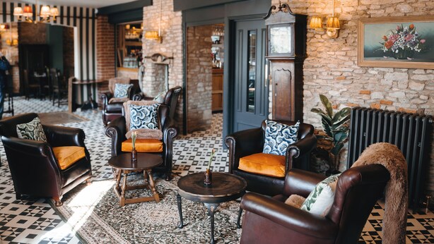 A cozy lounge area with leather armchairs, a patterned rug, and a vintage fireplace. - The Market Tavern (Bampton)