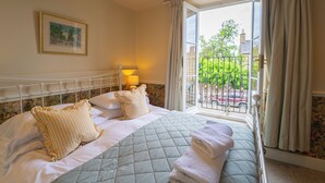 A hotel room with a bed, a window with curtains, a framed picture on the wall, and a balcony with a railing. - The Market Tavern (Bampton)