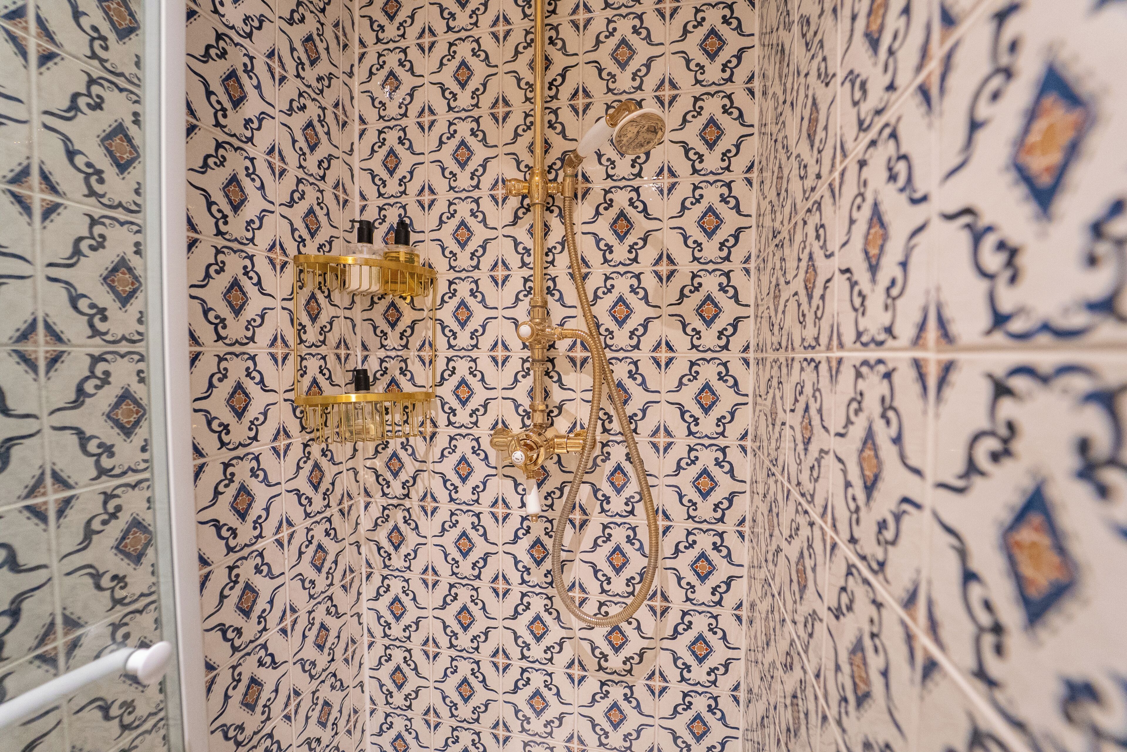 Un baño con baldosas estampadas y una ducha con detalles dorados.