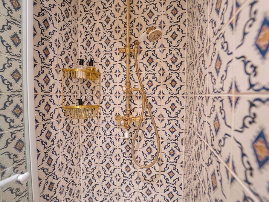 A bathroom with patterned tiles and a shower with a gold fixture.