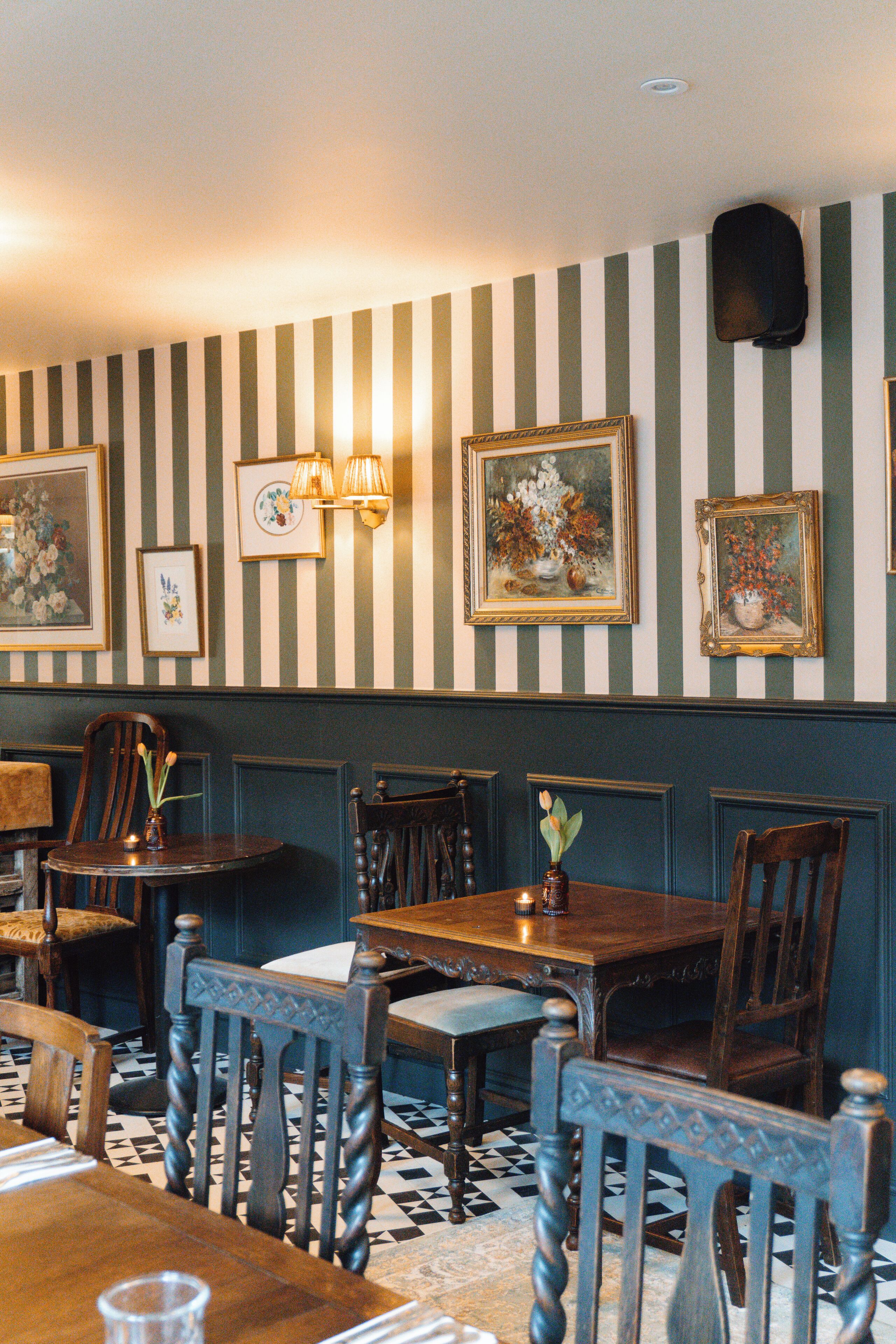 A dining area with striped wallpaper, wooden furniture, and framed artwork on the walls.