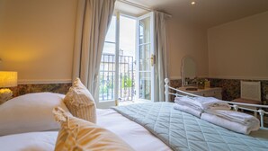 A hotel room with a bed, a dresser, a mirror, and a window with curtains. - The Market Tavern (Bampton)