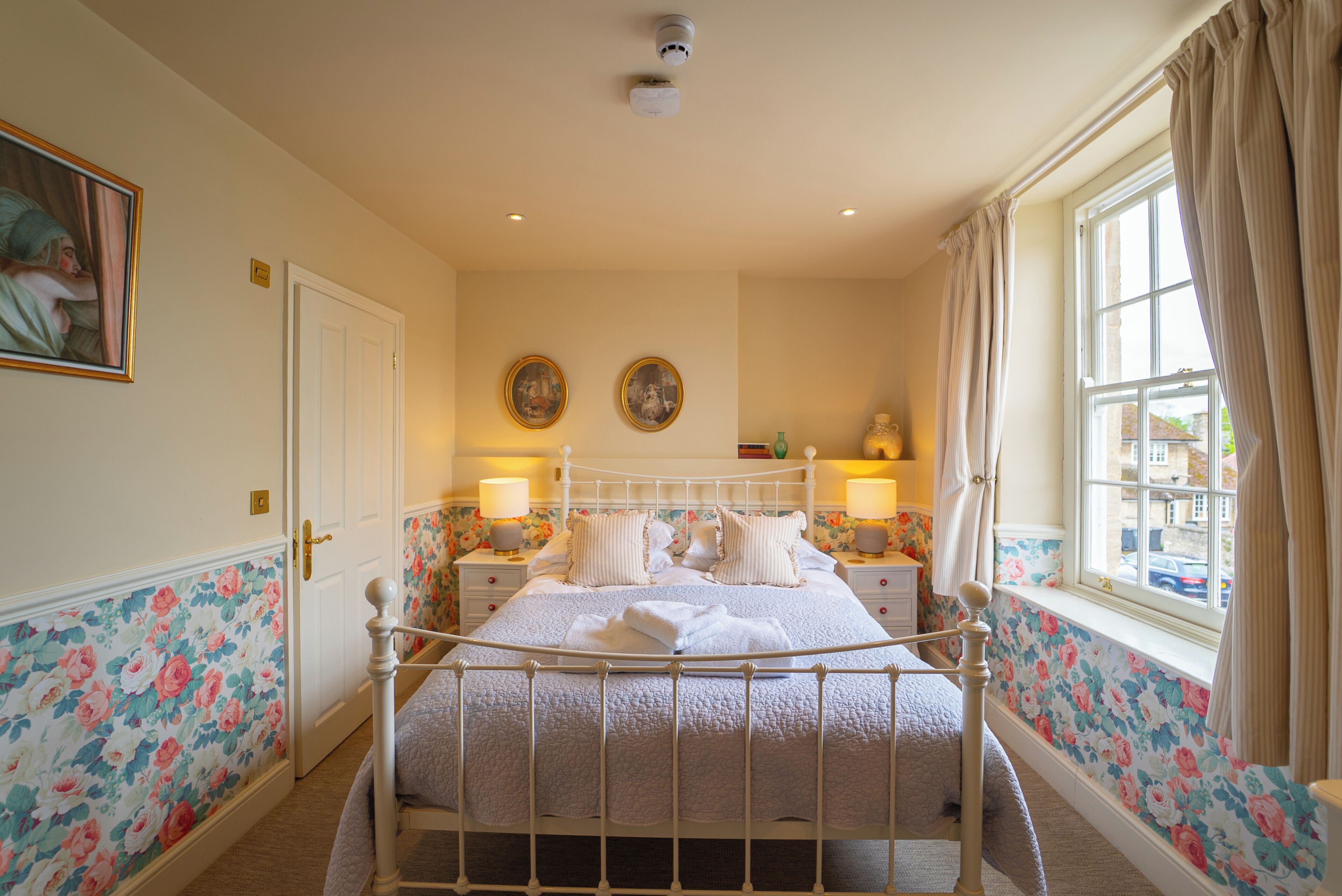 Een keurig opgemaakt slaapkamer met een bed, nachtkastjes en een raam met gordijnen.