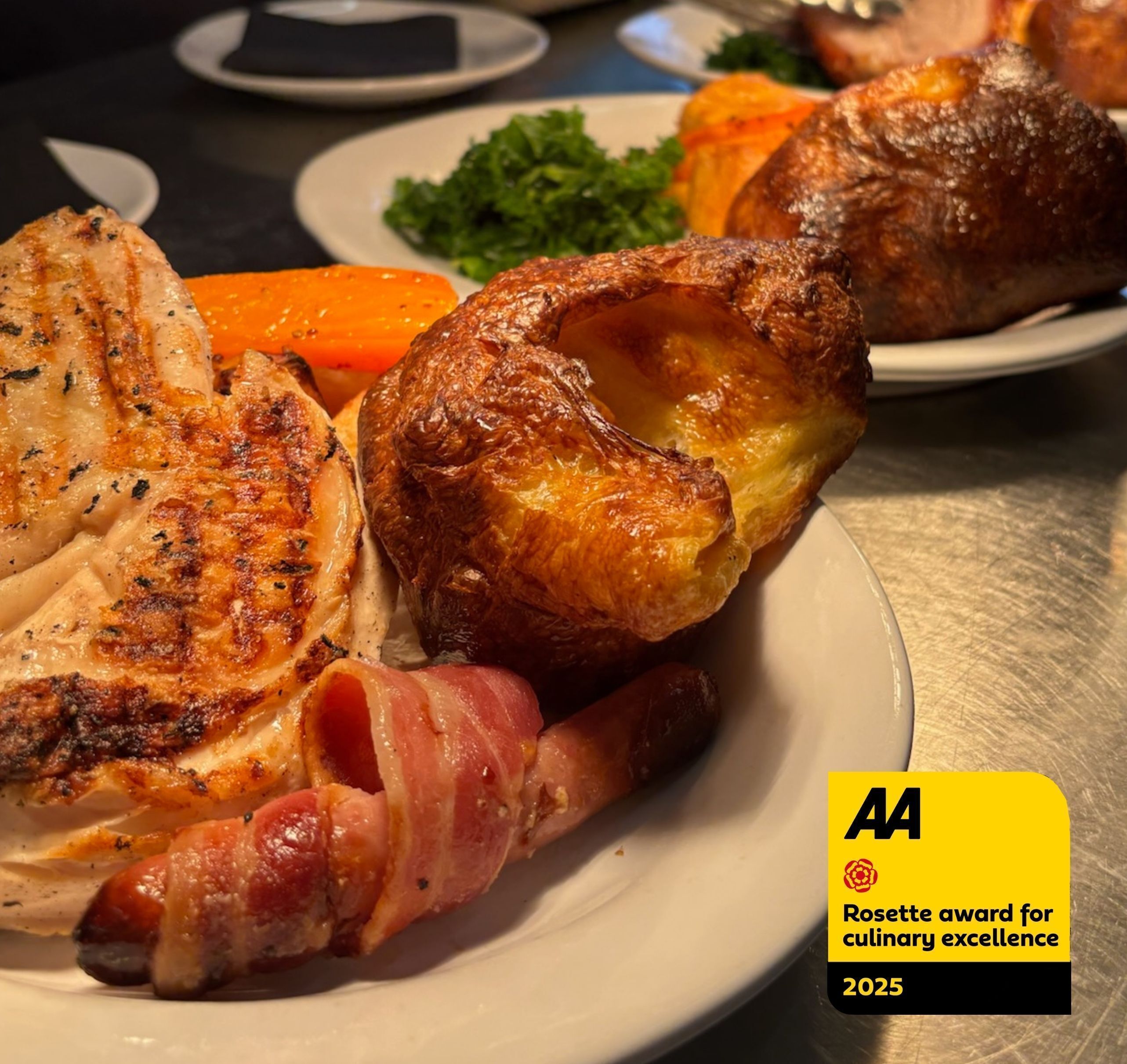 A plate of roasted chicken, carrots, and a Yorkshire pudding.