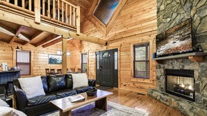 A cozy log cabin interior with a stone fireplace, wooden floors, a leather sofa, and a dining area. - Resort Pool Fitness Room Hot Tub Jacuzzi (Gatlinburg)