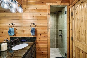 Baño de cabaña de madera con lavamanos, toalleros y ducha.