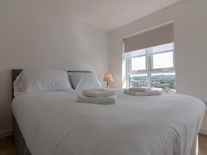 Een net opgemaakt bed met witte lakens en handdoeken, een bedlampje en een raam met uitzicht op het landschap.
