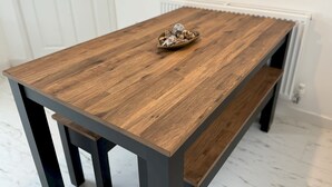 Una mesa de comedor de madera con un banco, ubicada en una habitación con paredes y puerta blancos.