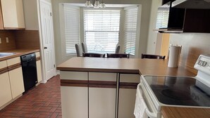 Una cocina con una isla central, lavavajillas, estufa y ventana con persianas.