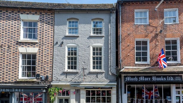 A row of traditional buildings with a mix of brick and stone facades, including a shop with British flags and a sign for 'Much More Books Ltd.' - Pass the Keys | Bright and cosy flat in the centre of Much Wenlock (Much Wenlock)