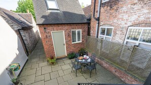 A small brick house with a tiled patio, a table set for tea, and a bicycle. - Pass the Keys | Bright and cosy flat in the centre of Much Wenlock (Much Wenlock)