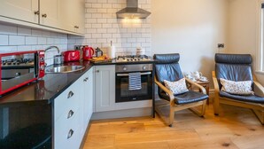 A compact kitchen with white cabinets, a black countertop, a red toaster, a kettle, and a gas stove. There are two leather chairs with cushions. - Pass the Keys | Bright and cosy flat in the centre of Much Wenlock (Much Wenlock)