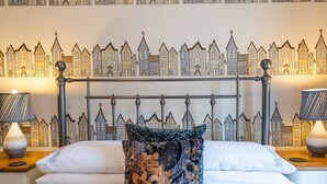 A neatly made bed with white linens and a floral-patterned pillow, set against a wall with a cityscape wallpaper. - Pass the Keys | Bright and cosy flat in the centre of Much Wenlock (Much Wenlock)