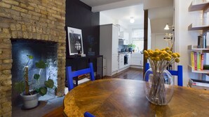 A dining area with a wooden table, blue chairs, a vase with yellow flowers, and a brick wall. - Stylish Garden Apartment in Vibrant Leyton - Pass the Keys (London)