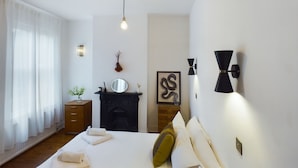 A bedroom with a bed, bedside table, mirror, wall art, and a fireplace. - Stylish Garden Apartment in Vibrant Leyton - Pass the Keys (London)