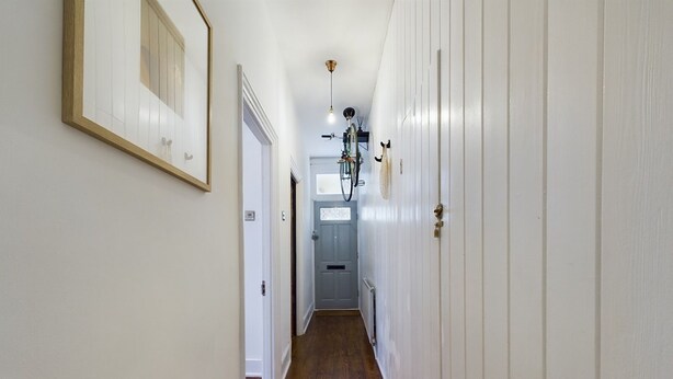 Un couloir étroit avec un plancher en bois, des murs blancs et une porte au fond.
