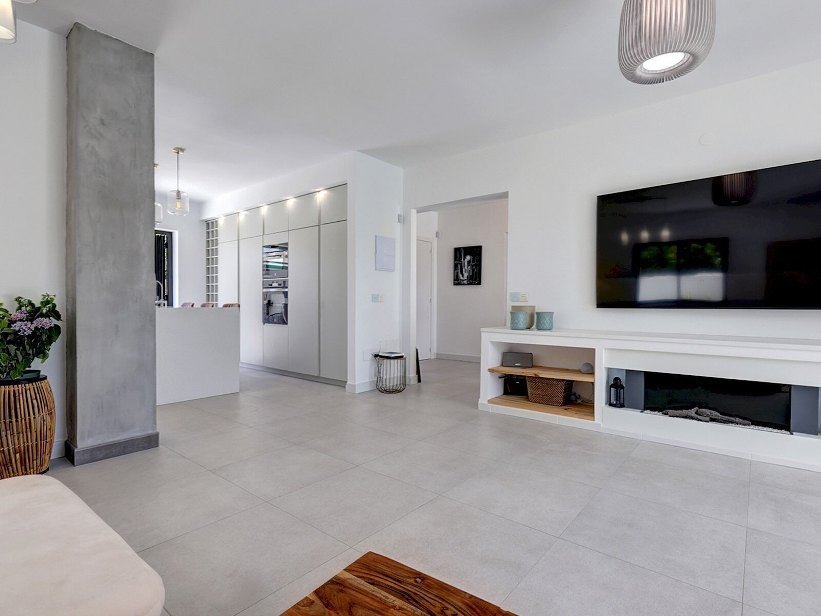 A modern living room with a large flat-screen TV, a white entertainment unit, and a concrete pillar.