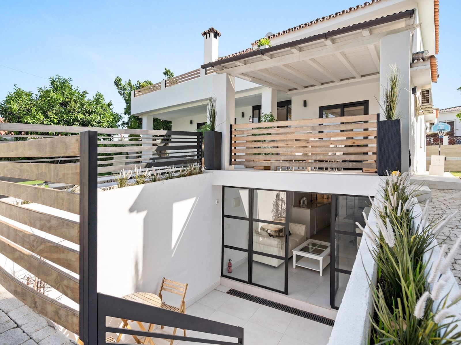 A modern two-story house with a balcony, large windows, and a patio area.