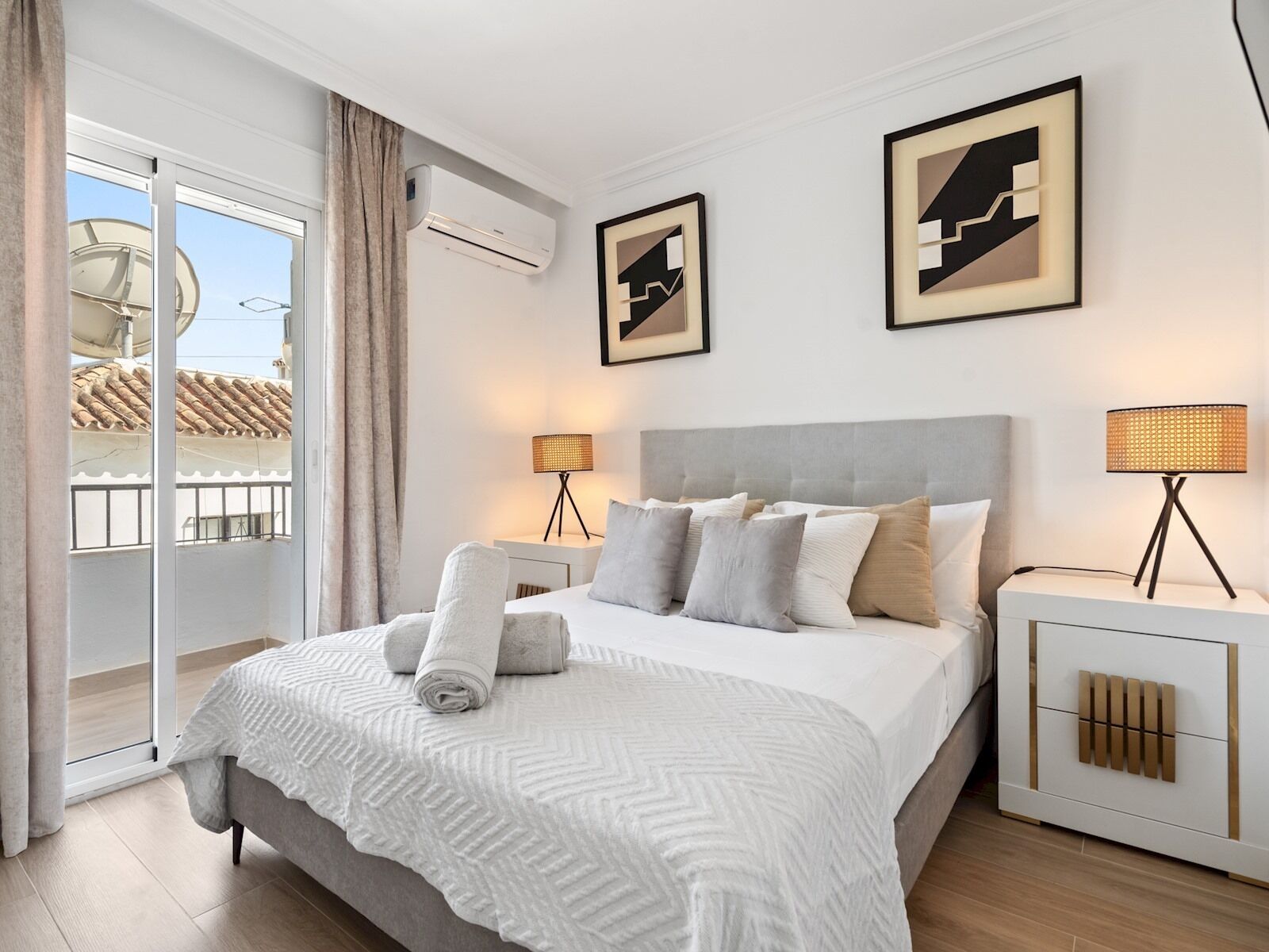 A modern hotel room with a large bed, a bedside table, a lamp, and a wall-mounted air conditioner.