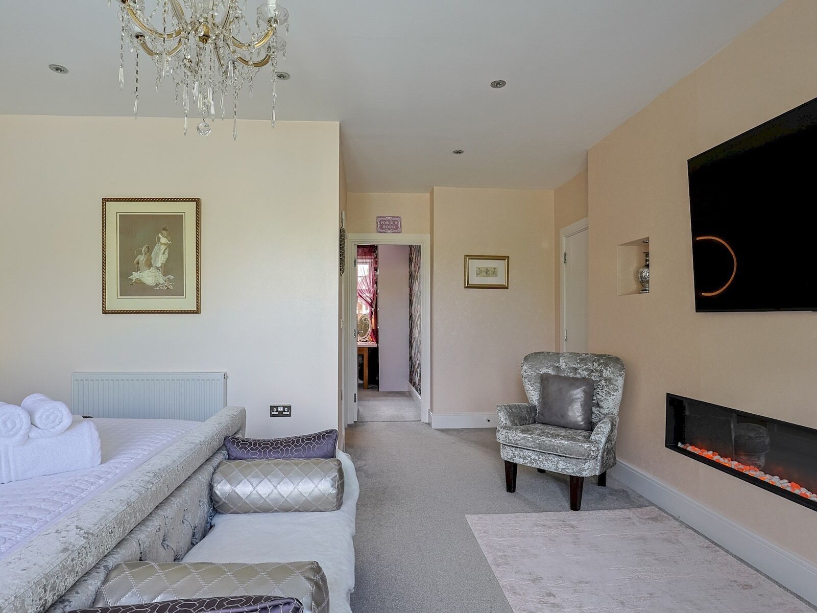 A bedroom with a bed, a chair, a fireplace, and a chandelier.