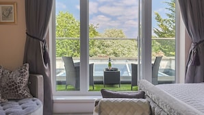 Une chambre avec une grande fenêtre, un lit, une chaise et une petite table sur laquelle se trouvent une bouteille et un verre.